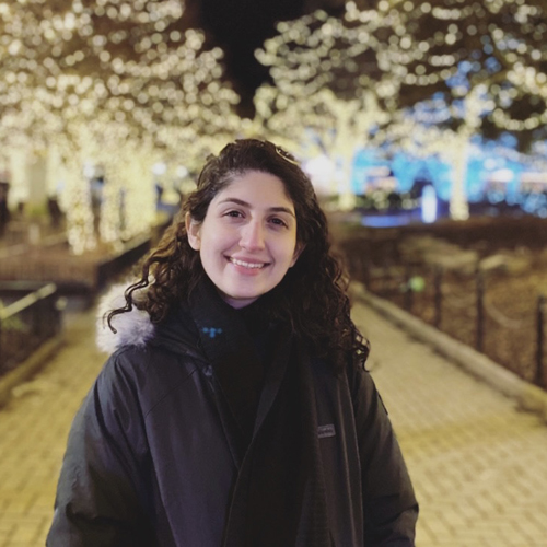 Fatima Ghaderi looking directly at the camera in front of lit up trees