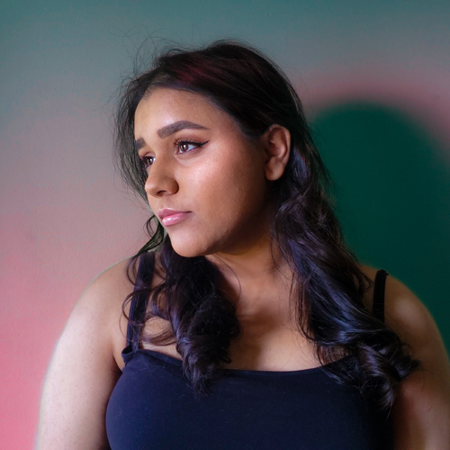 Fizza Ahmed looking off to the left in front of a pink and green background