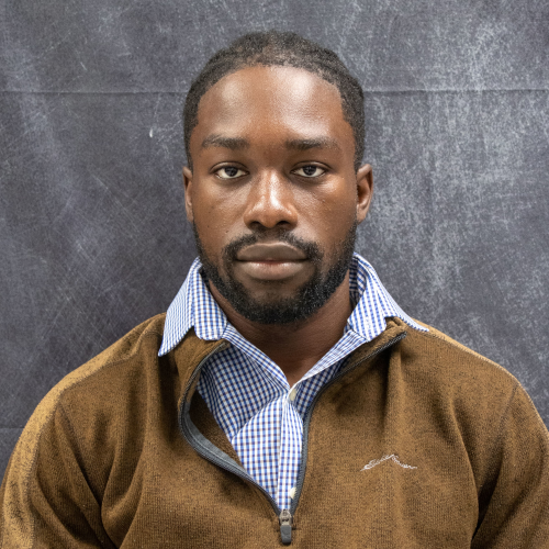 James Esemu-Ezewu looking directly at the camera in front of a gray bckground