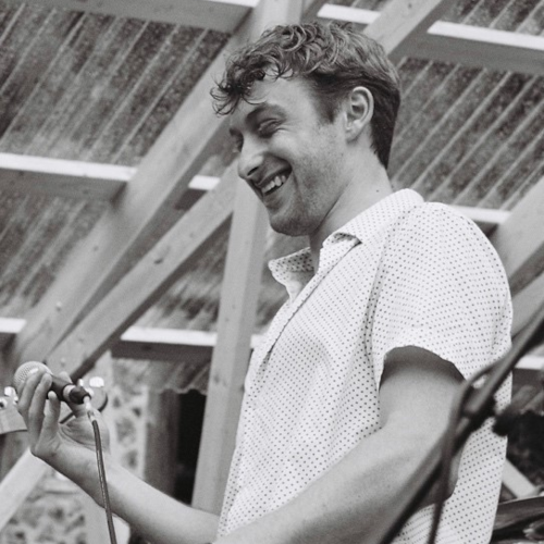 Zeke Wilson, holding a microphone, on stage, smiling